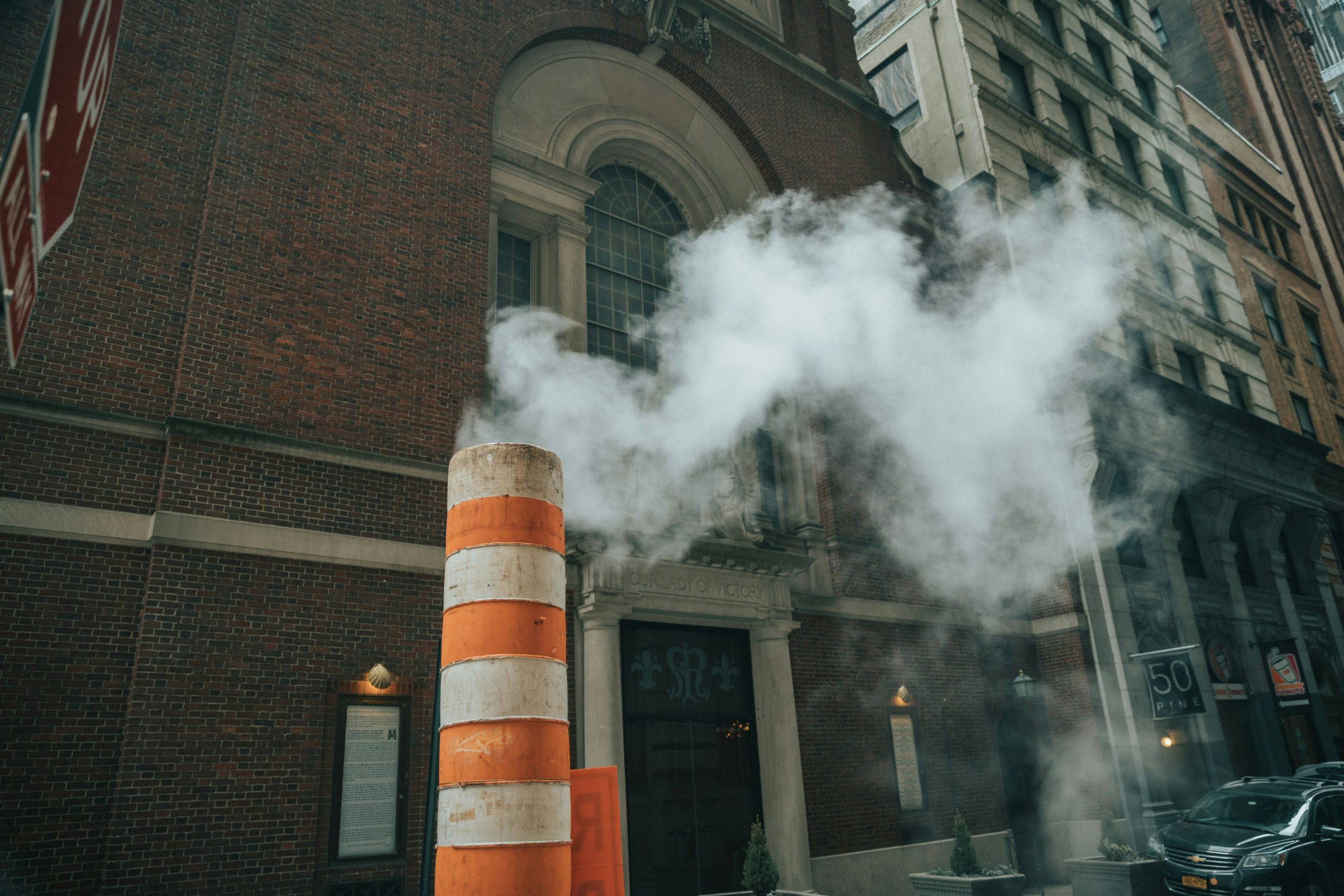 Smoke billowing from a striped construction pipe near a brick building, illustrating urban air quality concerns relevant to smoke odor elimination services by Restoration Experts.