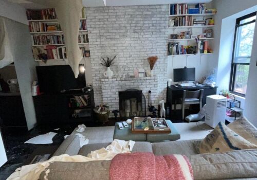 Bringing Life Back: Complete Restoration After Water Damage Living room with water damage, collapsed ceiling, exposed structural issues, and cluttered furniture, highlighting the need for restoration and repair services.